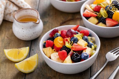 Böğürtlen, narenciye, nane ve bal soslu ahşap bir masada meyve salatası.