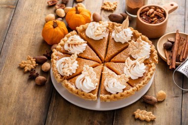 Traditional pumpkin pie for Thanksgiving cut into slices with whipped cream and leaf shaped decorations clipart