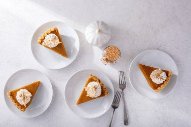 Şükran Günü için geleneksel balkabağı turtası. Krema ve yaprak şekilli süslemeler beyaz masada dilimlenmiş.