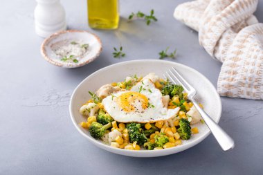 Sağlıklı kahvaltı kasesi, pişmiş sebze ve kızarmış yumurta karnabahar, brokoli ve mısırla birlikte.