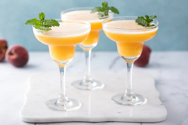 Frozen peach margaritas in three glasses garnished with mint