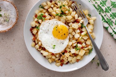 Kızarmış yumurta ve taze otla kaplanmış pancetta soslu patates kızartması.