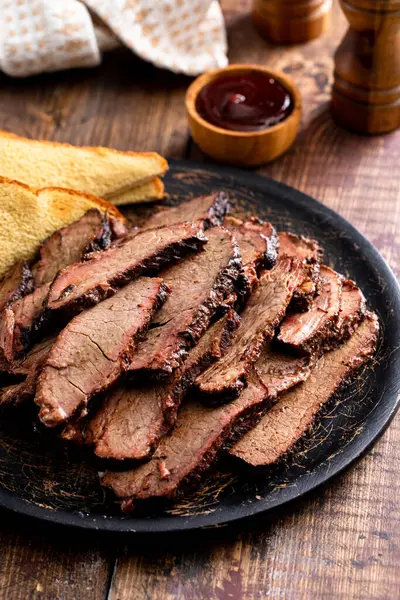 Sliced smoked brisket on a serving plate with toast served with BBQ sauce