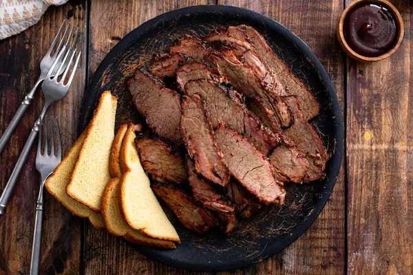 Sliced smoked brisket on a serving plate with toast served with BBQ sauce
