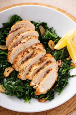 Dilimlenmiş tavuk göğsü sotelenmiş sarımsaklı ıspanak ve limon, sağlıklı öğle yemeği fikri.