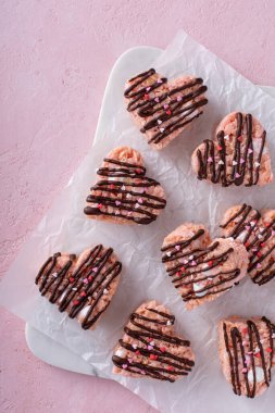 Pembe kalp şeklinde pirinç gevrekleri serinletici rafta koyu çikolata serpiştirilmiş, mermer bir tahtanın üzerinde ev yapımı tatlı ikram