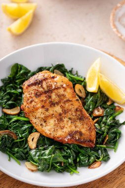 Izgara tavuk sotelenmiş ıspanak, sarımsak ve limon dilimleri ile servis edilir.