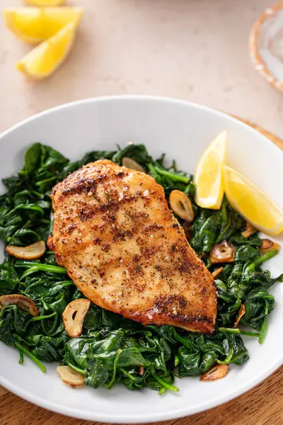 Izgara tavuk sotelenmiş ıspanak, sarımsak ve limon dilimleri ile servis edilir.