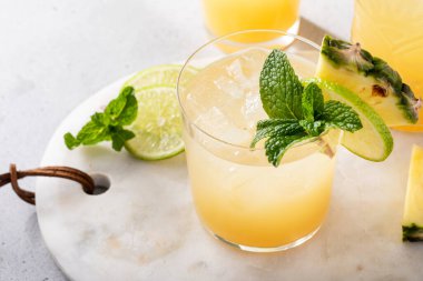 Bir dilim ananas ve nane yaprağıyla süslenmiş limonlu ananas suyu kokteyli.