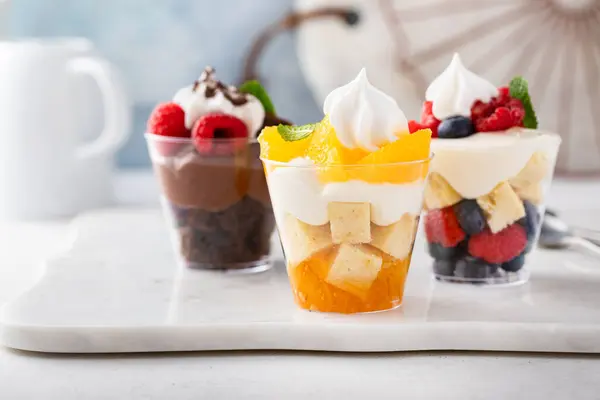 Three desserts in cups, variety of trifles with orange, chocolate and berry cakes