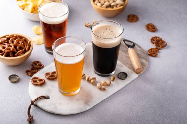 Koyu siyah bira, bira ve bira masada uzun bardaklarda, çeşitli biralar atıştırmalıklar, krakerler ve cipsler.