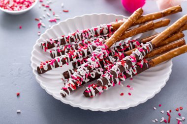 Çikolata soslu çubuk kraker, siyah beyaz çikolata ve tabağa pembe kalp serpiştirilmiş.