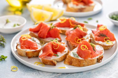 Krem peynirli, dereotlu ve limonlu füme somon crostini servis tabağında.