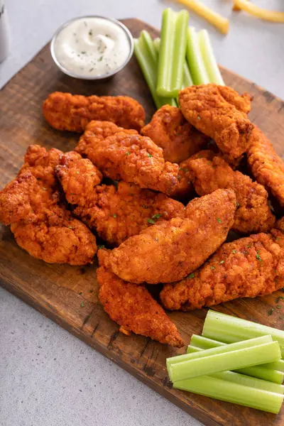 Buffalo fried chicken strips on a board with ranch and celery sticks