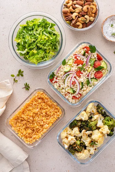 Healthy vegan meal prep with roasted vegetables, cooked lentils, couscous salad and mixed nuts