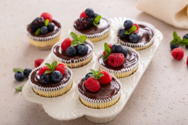 Mini vanilyalı New York peynirli kekleri kek tepsisinde pişirildi. Üstünde çikolata ganache ve taze böğürtlen var.