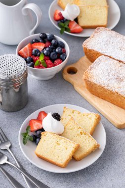 Geleneksel vanilyalı kek dilimlenmiş ve krem şanti ve taze böğürtlenlerle servis edilmiş.