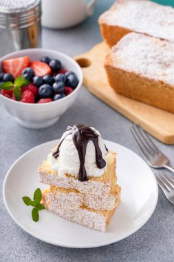 Geleneksel vanilyalı kek dilimlenmiş ve dondurma ve taze böğürtlenlerle servis edilmiş.