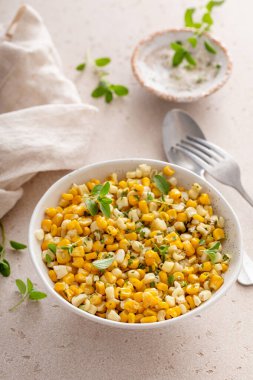 Hafif bir masada taze otlarla süslenmiş bir kase mısır salatası.