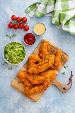 Fried chicken tenders on a serving board served with sauces and salad clipart