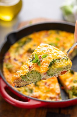 Sağlıklı frittata veya brokoli ve kırmızı biberli kiş dilimi, çedar peyniri ve domuz pastırması ile kaplanmış, dökme demir bir tavada pişirilmiş.