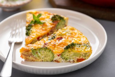 Sağlıklı frittata ya da brokoli ve kırmızı biberli kiş dilimi, çedar peyniri ve domuz pastırması ile kaplı, dökme demir bir tavada pişirilmiş, bir tabakta dilimlenmiş.