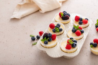 Mini vanilyalı New York peynirli kekleri taze böğürtlenlerle servis edilen kek tavasında pişiriliyor.