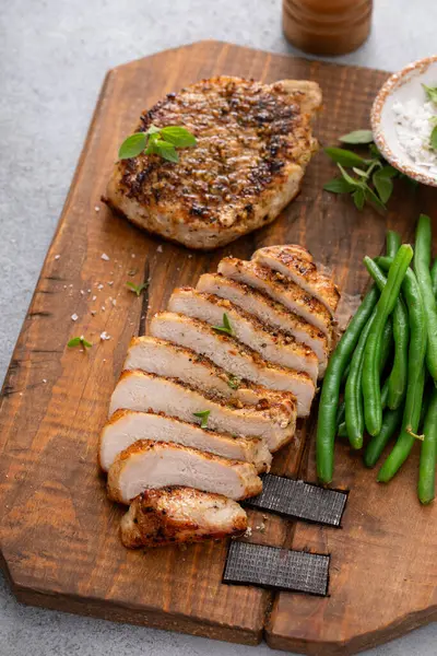 Izgara domuz pirzolası ya da yeşil fasulyeyle servis edilen kesme tahtasının üzerinde dilimlenmiş tavuk.
