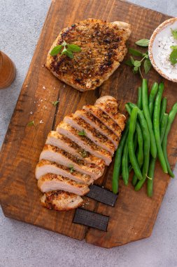 Izgara domuz pirzolası ya da yeşil fasulyeyle servis edilen kesme tahtasının üzerinde dilimlenmiş tavuk.