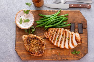 Izgara domuz pirzolası ya da yeşil fasulyeyle servis edilen kesme tahtasının üzerinde dilimlenmiş tavuk.