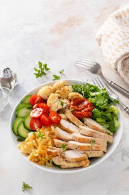 Kızarmış tavuk, kavrulmuş karnabahar, marul ve taze sebzeli sağlıklı yemek kasesi.