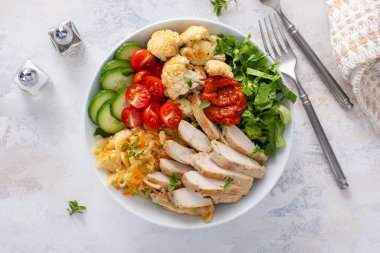 Kızarmış tavuk, kavrulmuş karnabahar, marul ve taze sebzeli sağlıklı yemek kasesi.