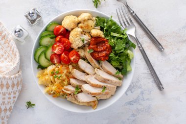 Kızarmış tavuk, kavrulmuş karnabahar, marul ve taze sebzeli sağlıklı yemek kasesi.