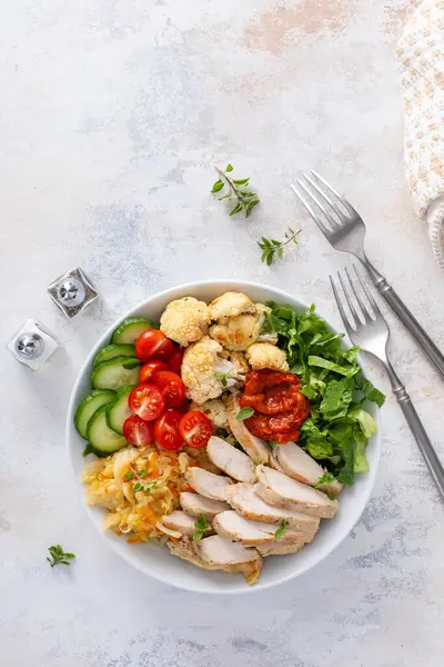 Kızarmış tavuk, kavrulmuş karnabahar, marul ve taze sebzeli sağlıklı yemek kasesi.