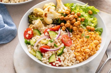 Mercimekli vejetaryen yemek kasesi, kızarmış sebze ve nohut, domatesli kuskus salatası ve salatalık, sağlıklı öğle yemeği fikri.