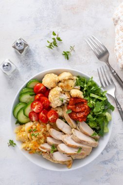 Kızarmış tavuk, kavrulmuş karnabahar, marul ve taze sebzeli sağlıklı yemek kasesi.