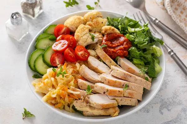 Kızarmış tavuk, kavrulmuş karnabahar, marul ve taze sebzeli sağlıklı yemek kasesi.