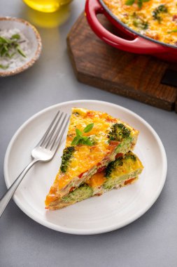 Brokoli, pastırma ve peynirli frittata dökme demir bir tavada iki dilimle pişiriliyor.