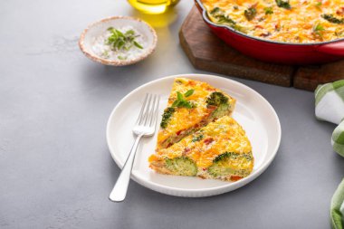 Brokoli, pastırma ve peynirli frittata dökme demir bir tavada iki dilimle pişiriliyor.