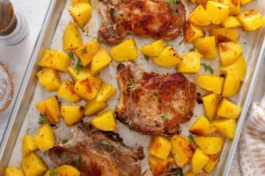 Kolay bir akşam yemeği için baharatlı ve otlu bir tavada kızartılmış domuz pirzolası ve patates.