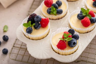 Taze böğürtlenlerle kaplı kek tavasında pişirilmiş mini peynirli kekler. Tatlı bir fikir.