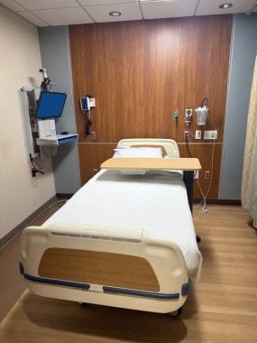 Ayarlanabilir yatak, tıbbi ekipman ve sakinleştirici ahşap dekorun olduğu temiz ve düzenli bir hastane odası. Sağlık ve tıbbi temalar için ideal.