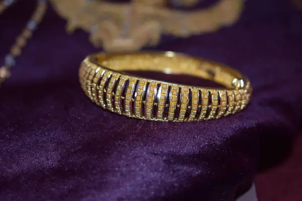 A stunning golden ring gleams, showcasing its elegant design and lustrous finish. golden bracelet rests on a rich purple velvet backdrop, highlighting its intricate details and radiant shine. Both pieces exude timeless luxury and sophistication.