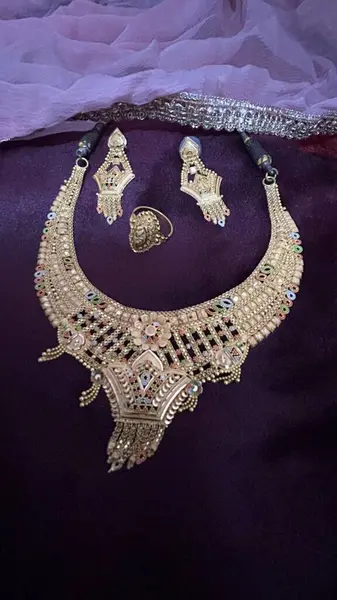 beautiful wedding rings, golden necklace, golden earrings on the velvet purple background, express love with golden jewelry. Perfect for wedding, engagement and anniversary. Indian Golden Jewlery gift ideas for women.