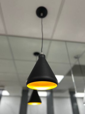 Yeni yenilenmiş bir banyoda asılı duran parlak, modern bir lamba, mekanın zarafetini artıran yumuşak bir ışık saçıyor. Yakın çekim, minimalist tasarımı yakalıyor ve banyo dekoruna çağdaş bir lüks katıyor.