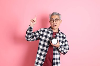 40 'lı yaşlarda Asyalı bir adam pembe arka planda sıradan kıyafetlerle dolanıyor..