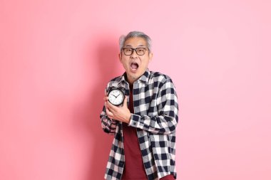 40 'lı yaşlarda Asyalı bir adam pembe arka planda sıradan kıyafetlerle dolanıyor..