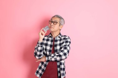 40 'lı yaşlarda Asyalı bir adam pembe arka planda sıradan kıyafetlerle dolanıyor..