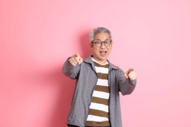 40 'lı yaşlarda Asyalı bir adam pembe arka planda sıradan kıyafetlerle dolanıyor..