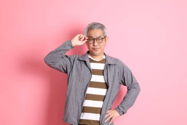 40 'lı yaşlarda Asyalı bir adam pembe arka planda sıradan kıyafetlerle dolanıyor..